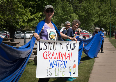 Image shows woman holding a sign that says "Listen to your grandma! Water is life."