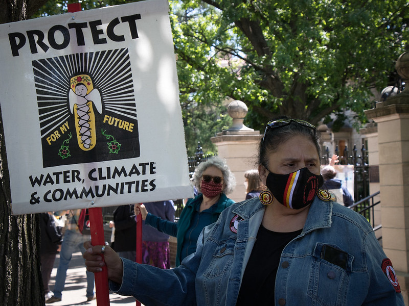 Image shows woman water protector holding a sign that says, "Protect water, climate and communities"